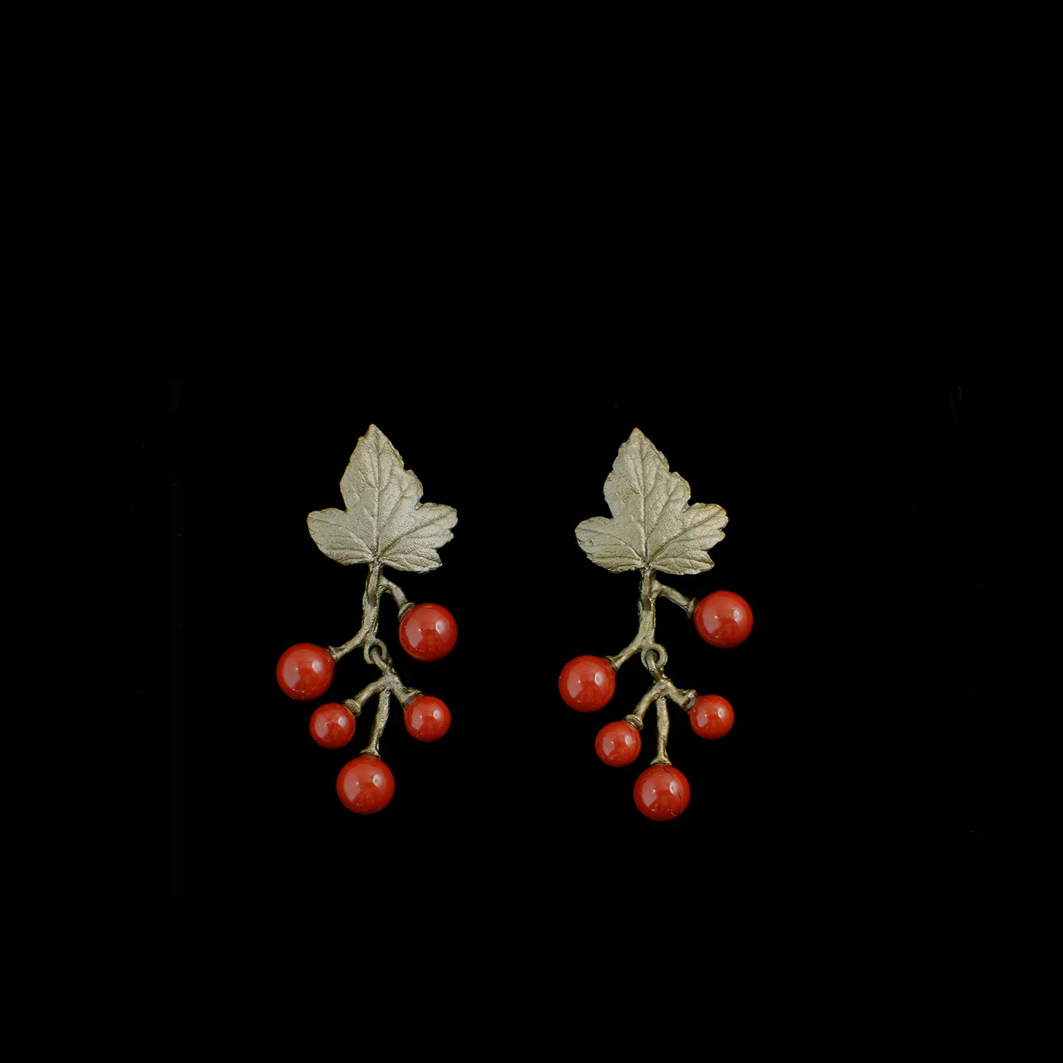 A pair of earrings shaped like leaves with branches, each holding five round red beads resembling berries, set against a black background.