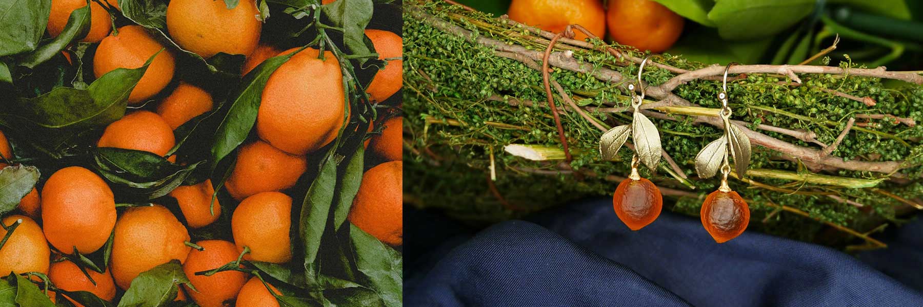 A pile of fresh oranges with green leaves next to a pair of orange-inspired earrings displayed on moss.