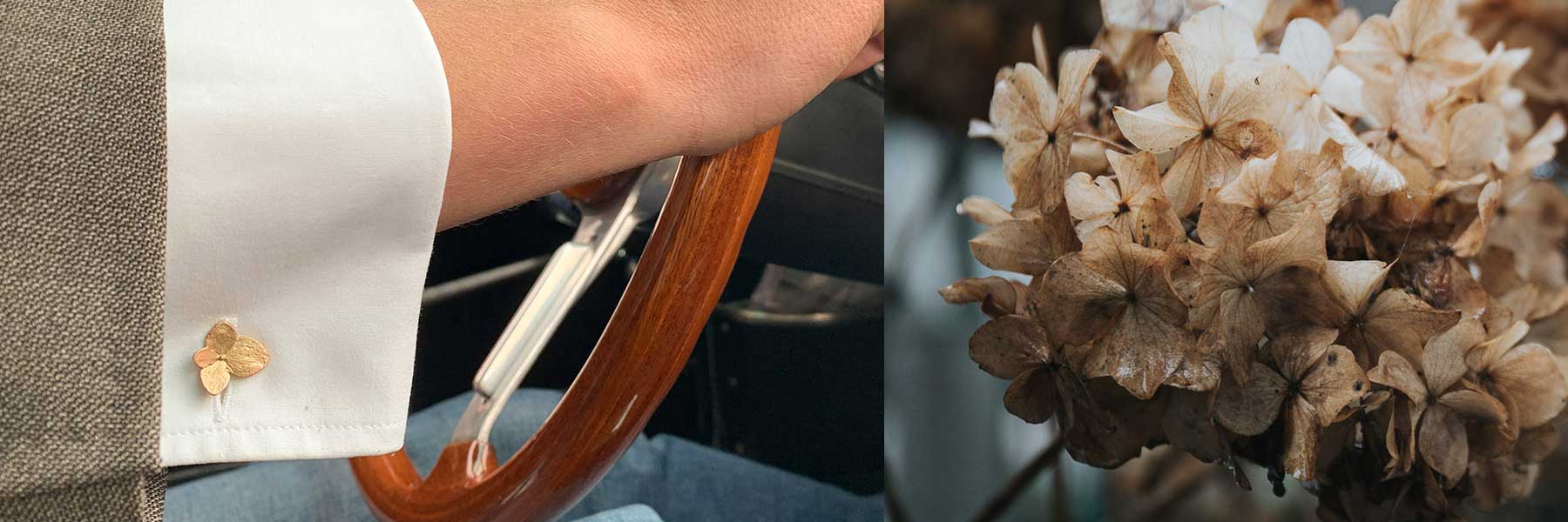 A close-up of a persons hand on a wooden steering wheel, wearing a white shirt with a gold flower-shaped cufflink, beside a cluster of dried beige flowers.