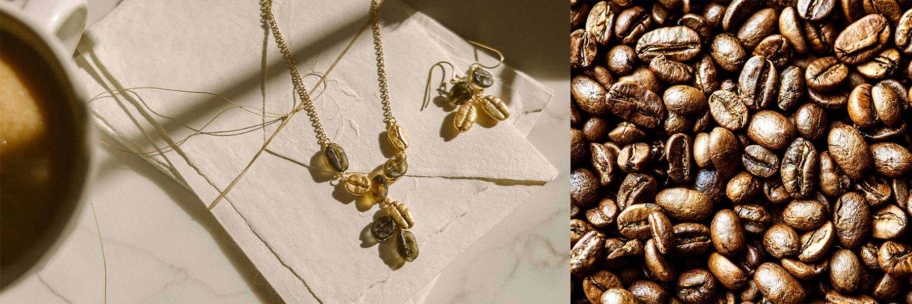 A gold necklace and earrings with coffee bean-shaped charms on napkins next to whole coffee beans and a cup of coffee.