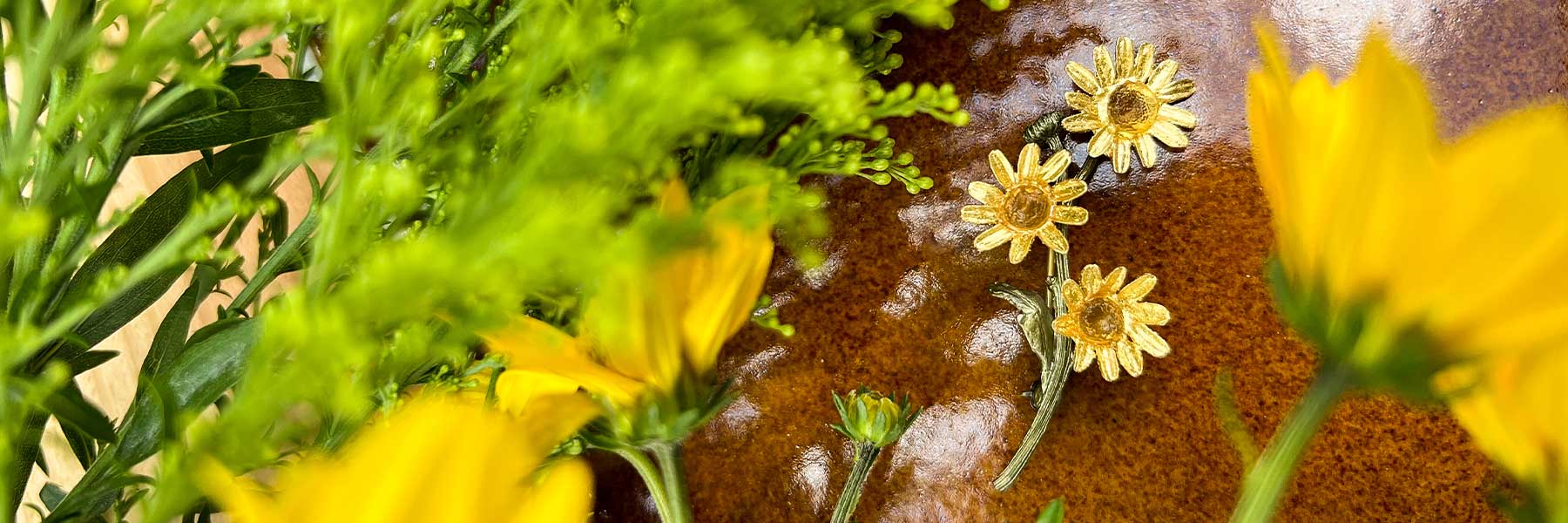 Yellow flowers and green foliage surround a brown ceramic surface decorated with small, yellow, flower-shaped ornaments.