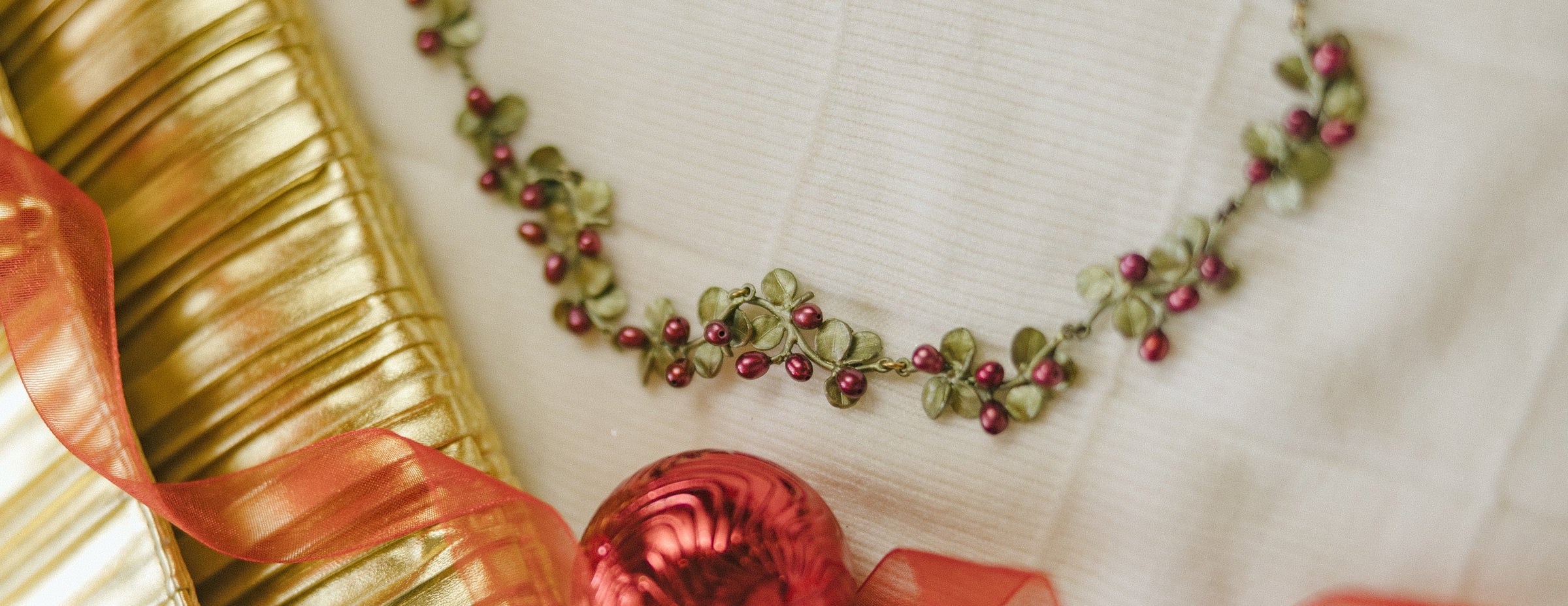A gold and red jeweled necklace displayed on a black box, surrounded by Christmas decorations, ornaments, ribbon, and greenery.