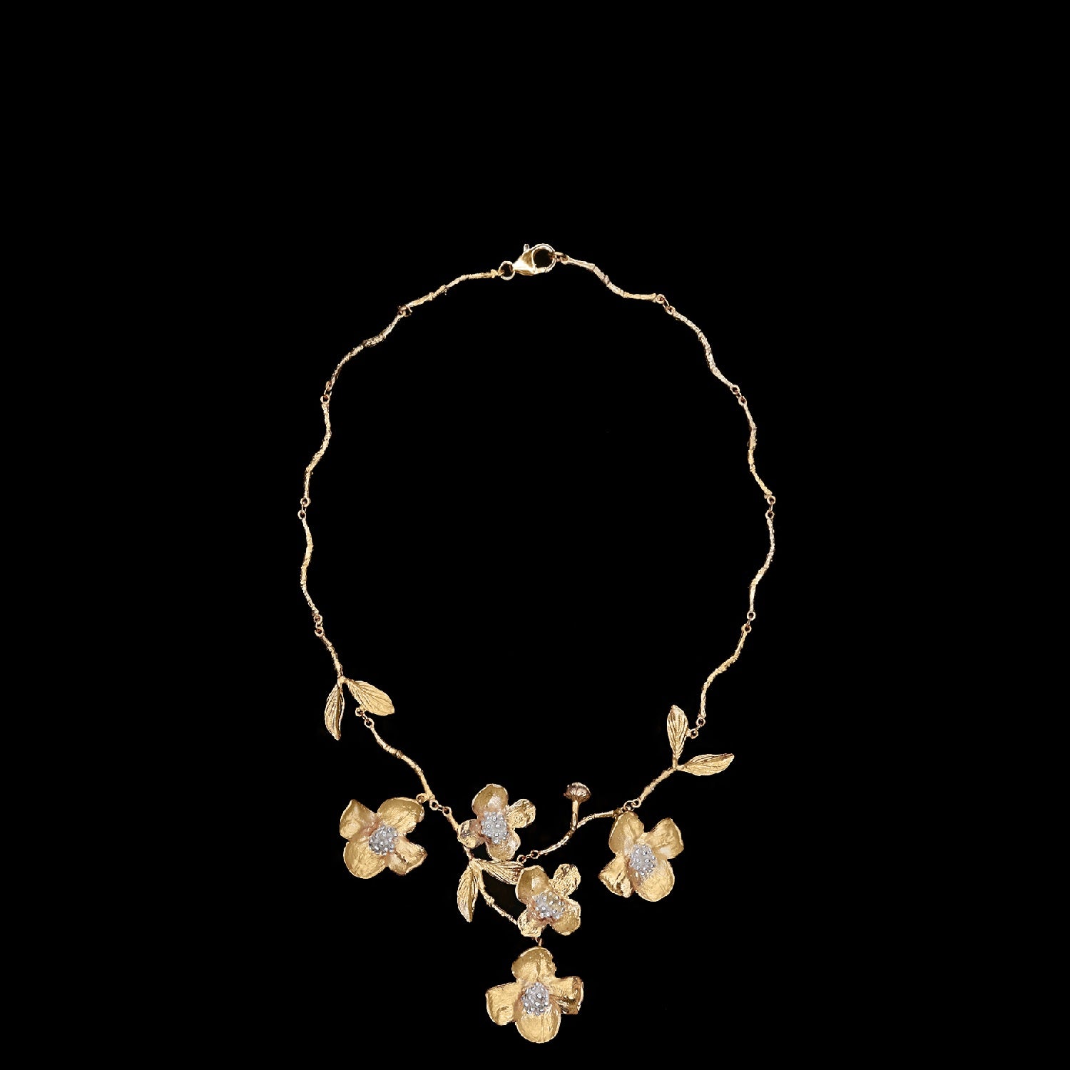 Gold necklace featuring a floral design with leaves and five flowers, each flower embellished with clear gemstones, displayed on a black background.