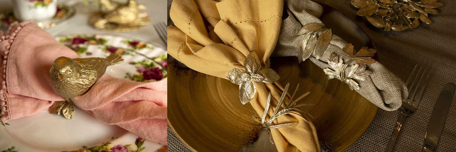 Dining table settings with gold-toned napkin rings shaped like a bird, leaves, and flowers, wrapping cloth napkins on floral and wooden plates.
