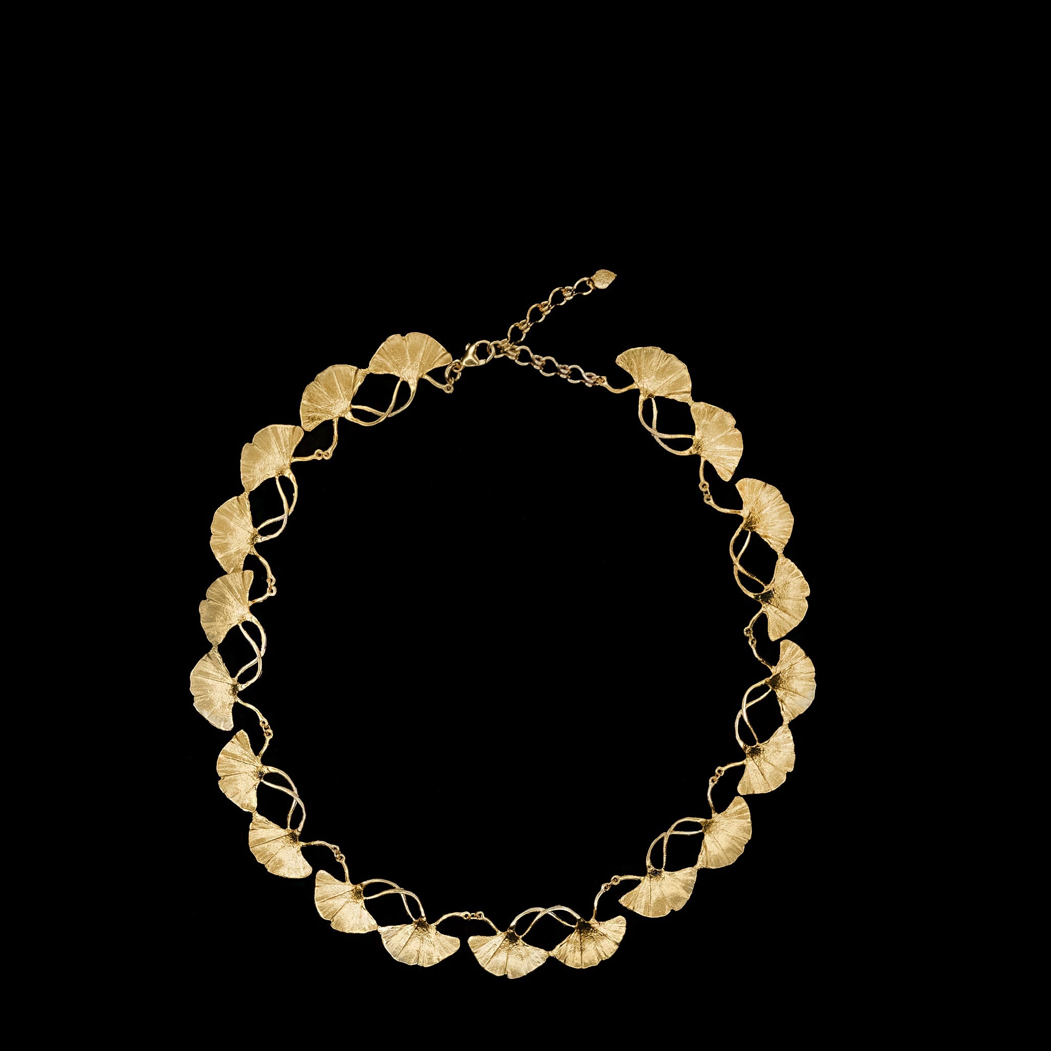Gold necklace featuring a series of leaf-shaped links connected in a circular pattern, displayed on a black background.