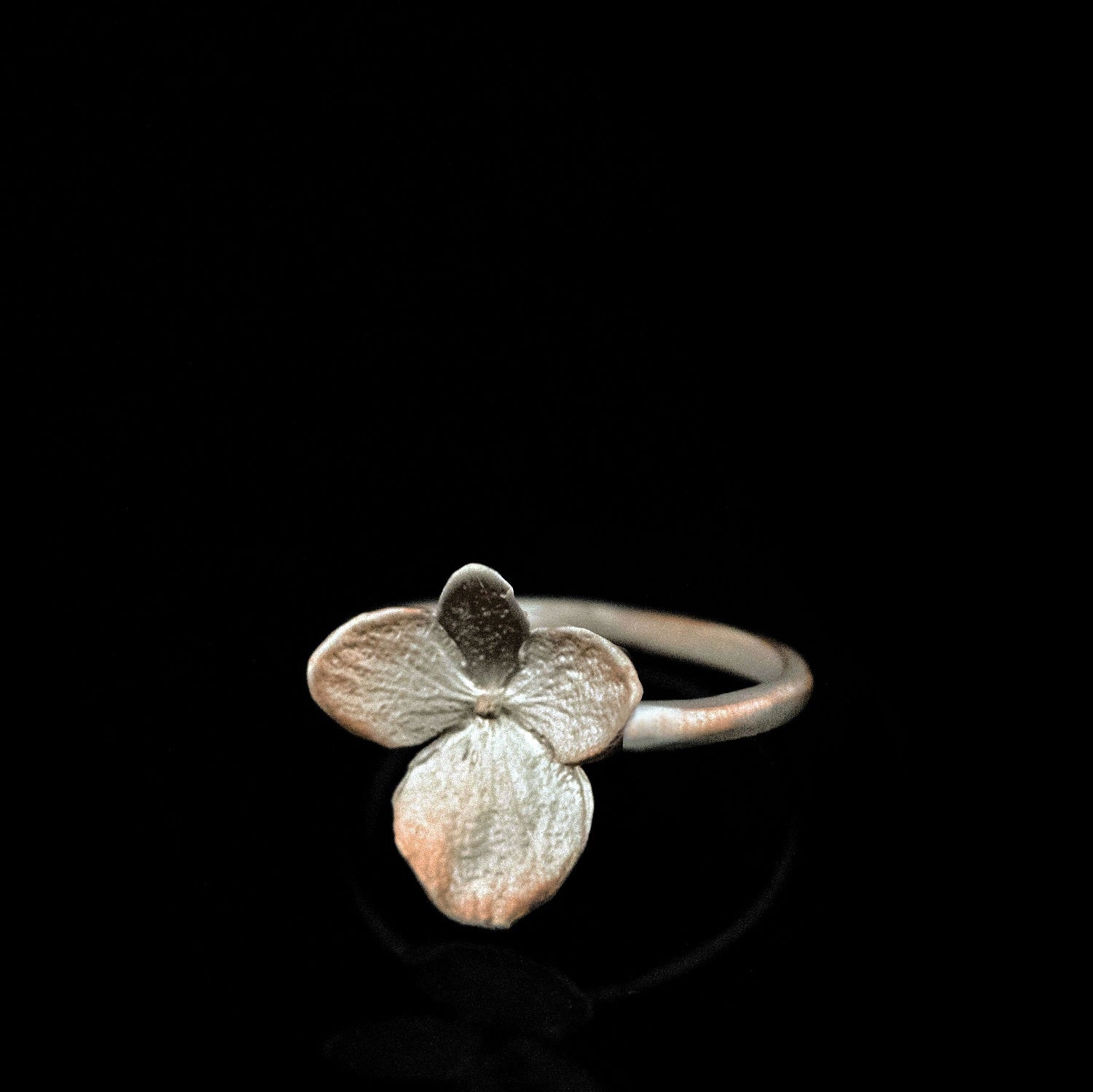 A silver ring featuring a delicate, three-petal flower design is displayed against a black background.