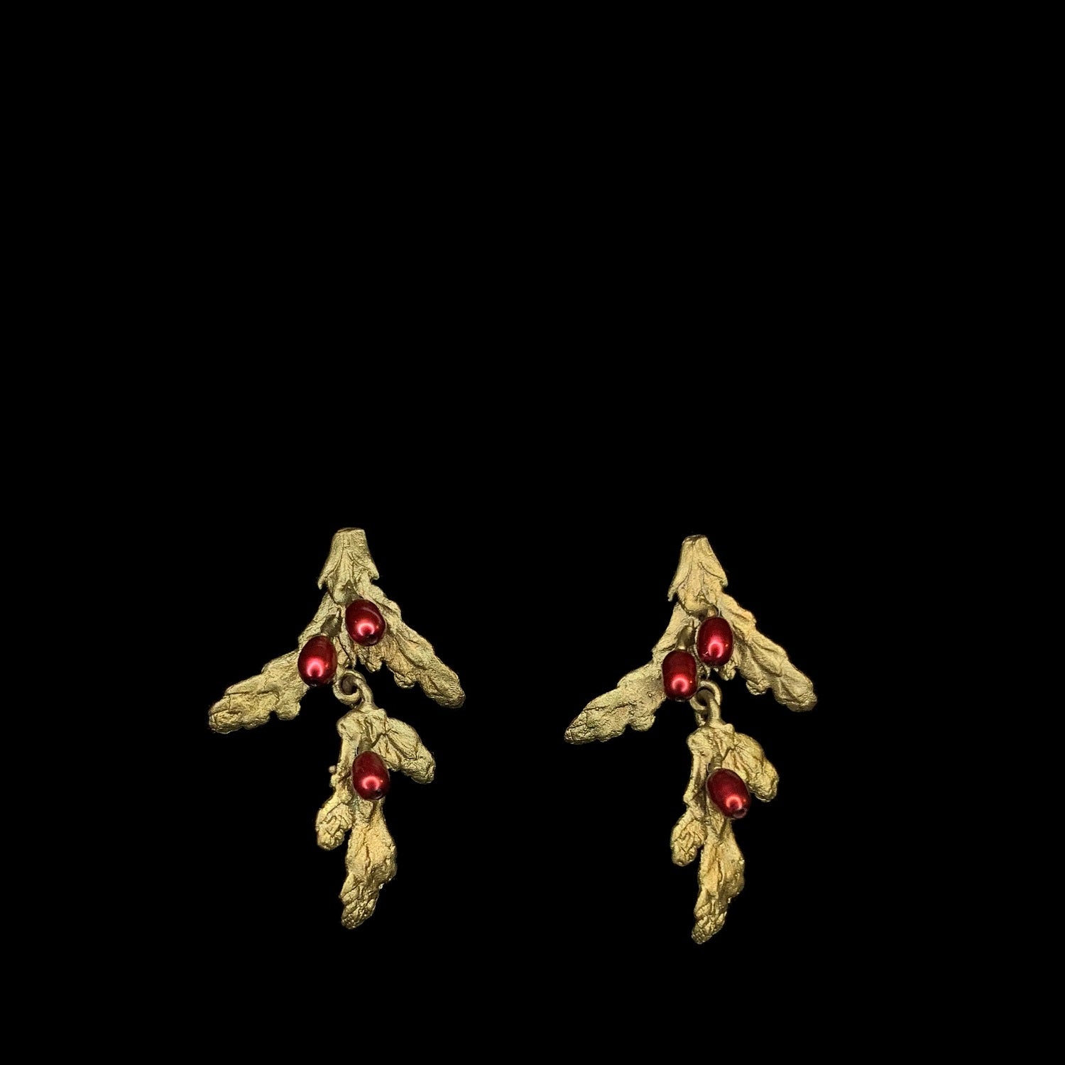 A pair of gold earrings shaped like branches with leaves, each featuring three small red beads resembling berries, displayed on a black background.