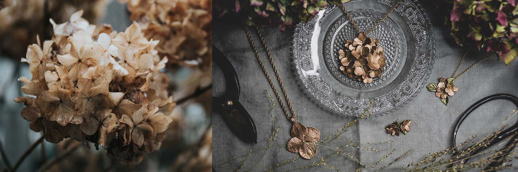 Dried hydrangea flowers on the left; on the right, gold jewelry pieces shaped like hydrangea petals displayed on a glass plate and gray fabric.