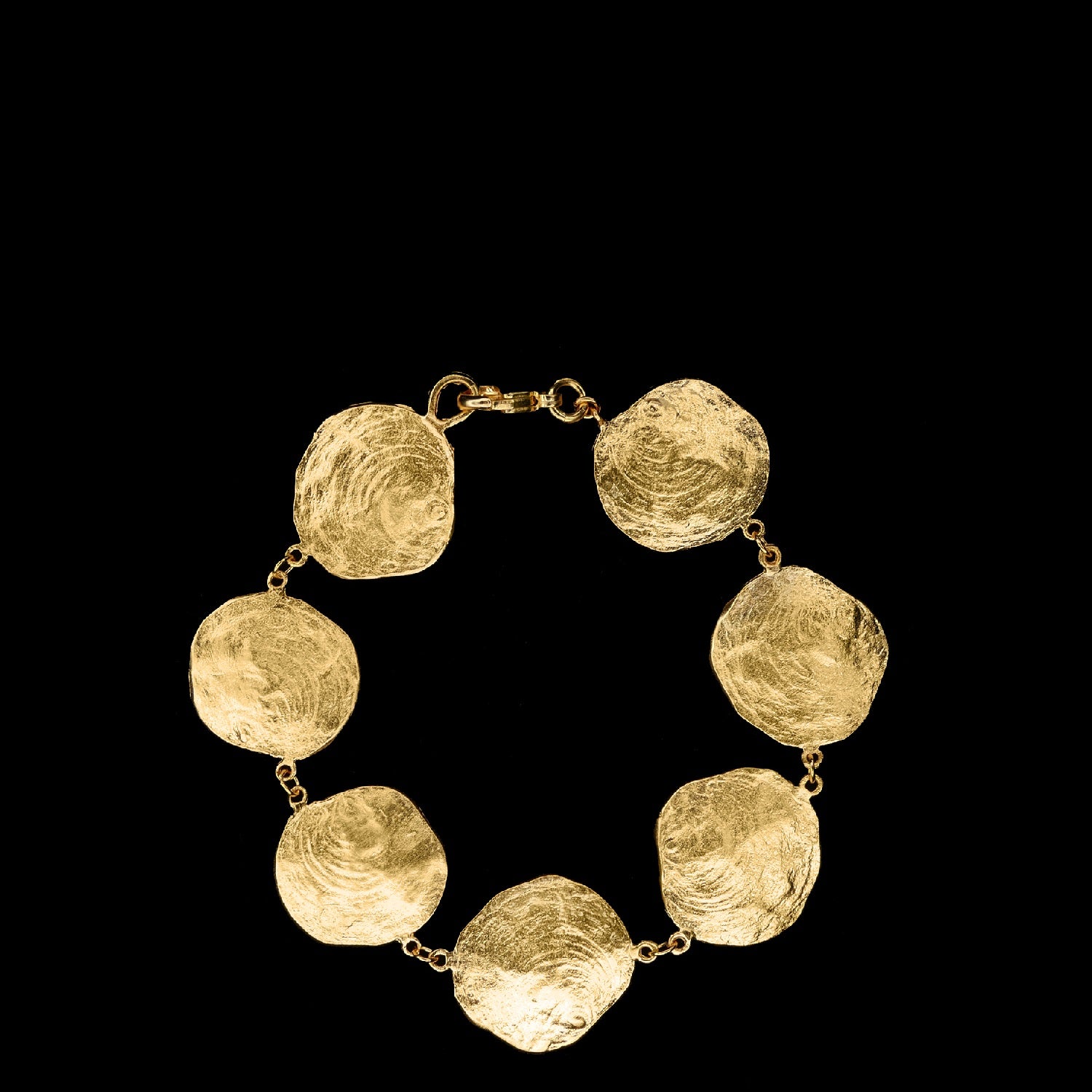 Gold bracelet featuring seven textured, round discs connected by small links, displayed on a black background.
