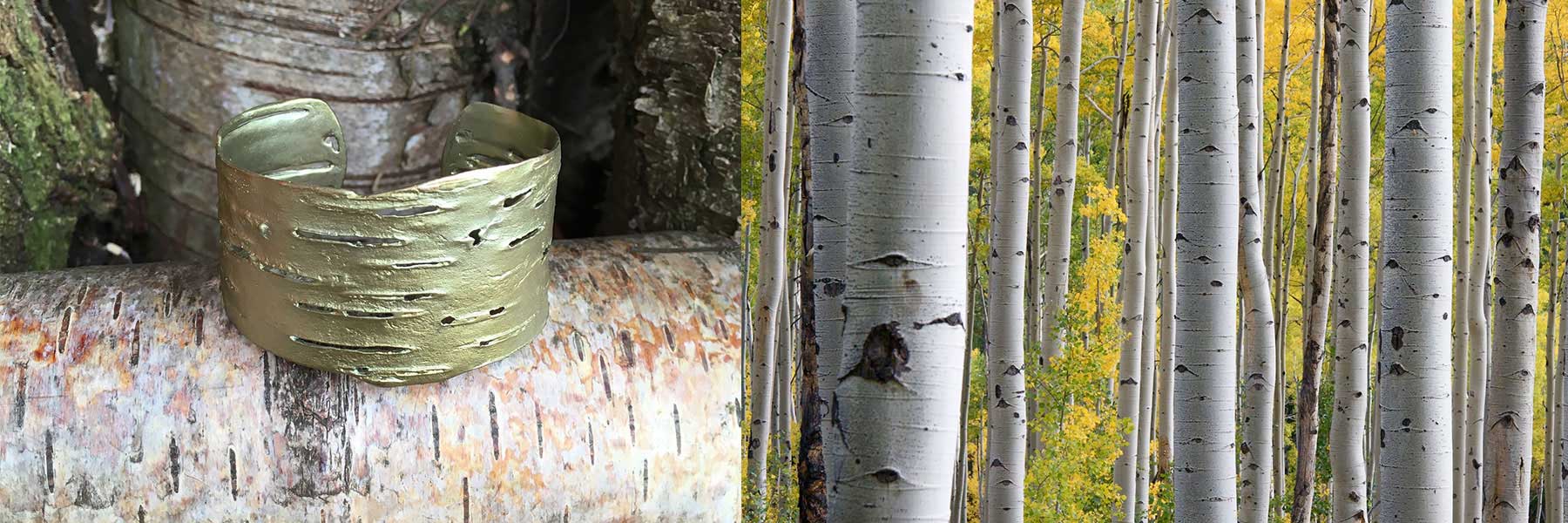 A gold cuff bracelet with a textured bark pattern rests on a birch log, next to a forest of tall, slender birch trees with yellow foliage.