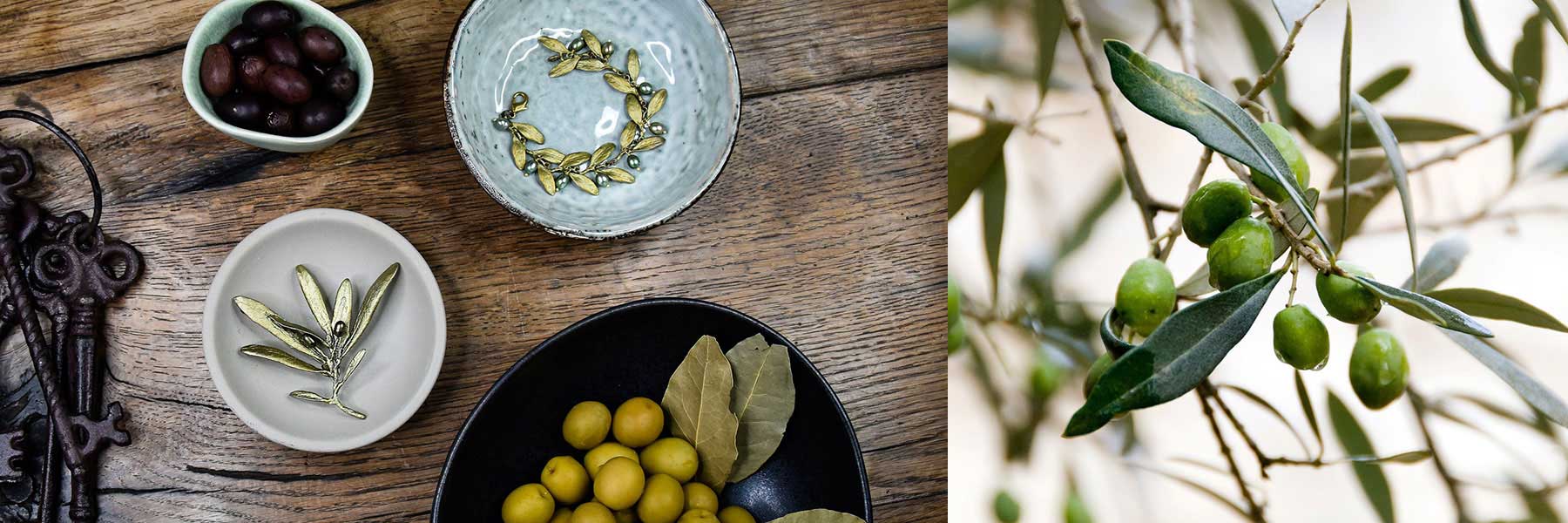 A top view of bowls with green and black olives, bay leaves, and olive-shaped metal ornaments on a wooden table; on the right, green olives growing on a tree branch.