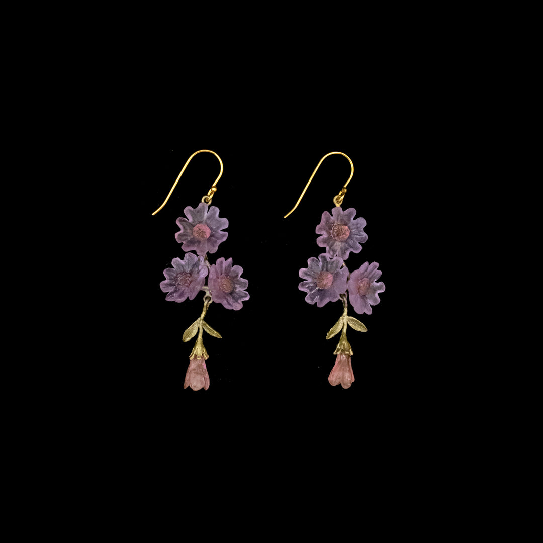 A pair of gold hook earrings featuring purple and pink flower designs with green leaf accents, displayed on a black background.