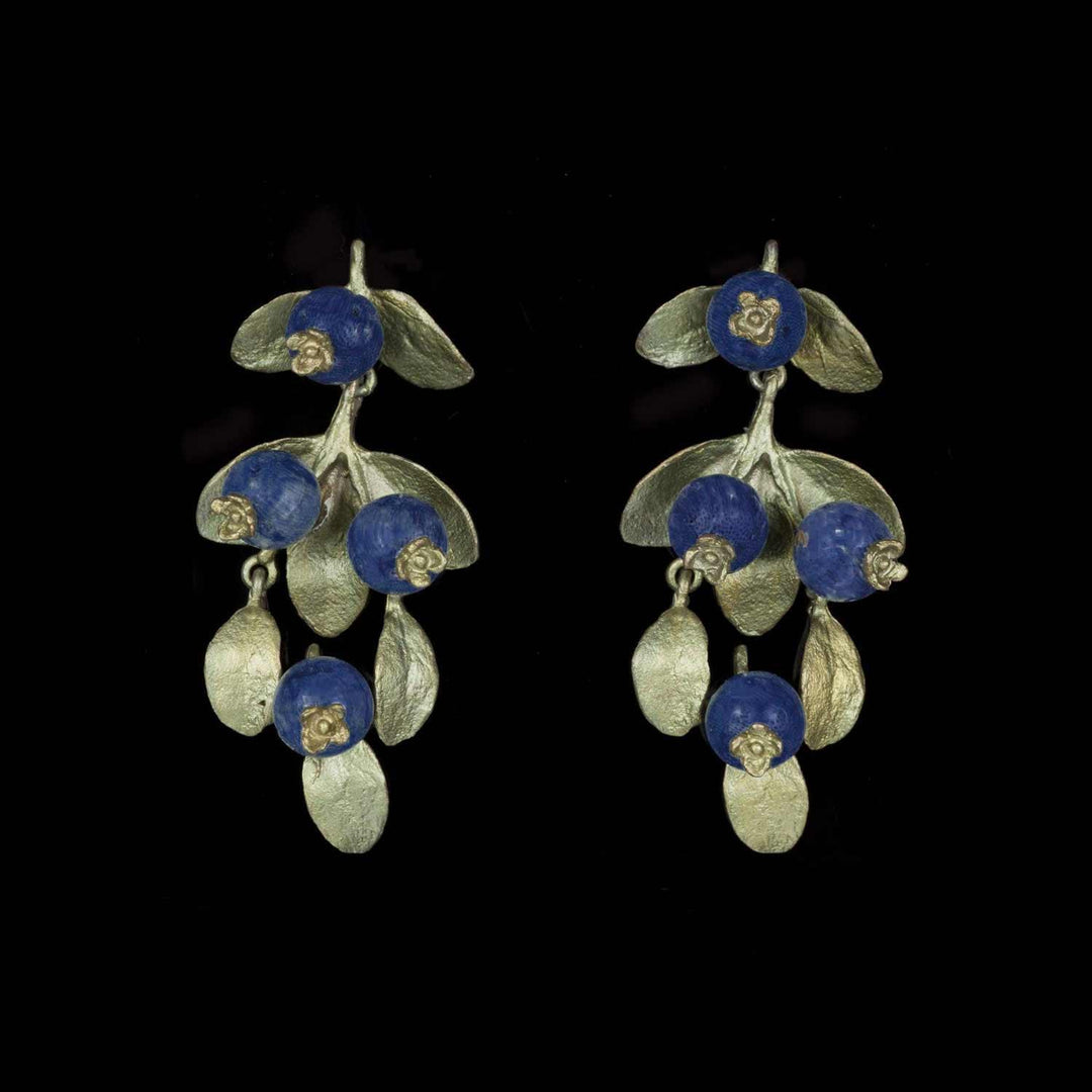 A pair of bronze earrings featuring blue lapis berries and green leaves against a black background.