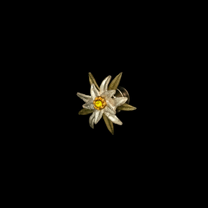 A metal pin shaped like an edelweiss flower with white petals, yellow center, and greenish leaves is displayed on a black background—perfect for fans of Sound of Music jewelry.