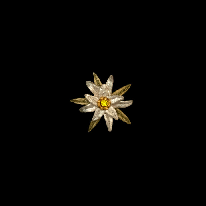 A metallic edelweiss flower pin with white petals, gold leaves, and a yellow gemstone center, reminiscent of iconic Sound of Music jewelry, displayed on a black background.