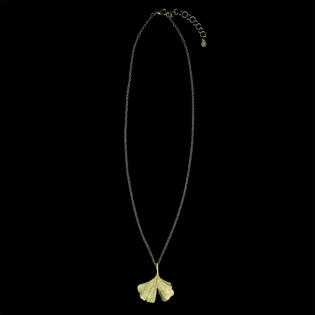 A green Ginkgo pendant necklace with a delicate leaf design, displayed on a black background and suspended from a brass chain.