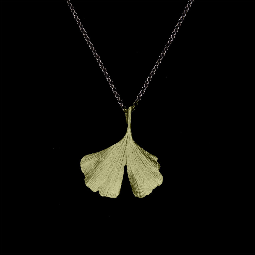 A silver necklace with a hand patinated bronze Ginkgo pendant, shaped like a textured ginkgo leaf, displayed against a black background.