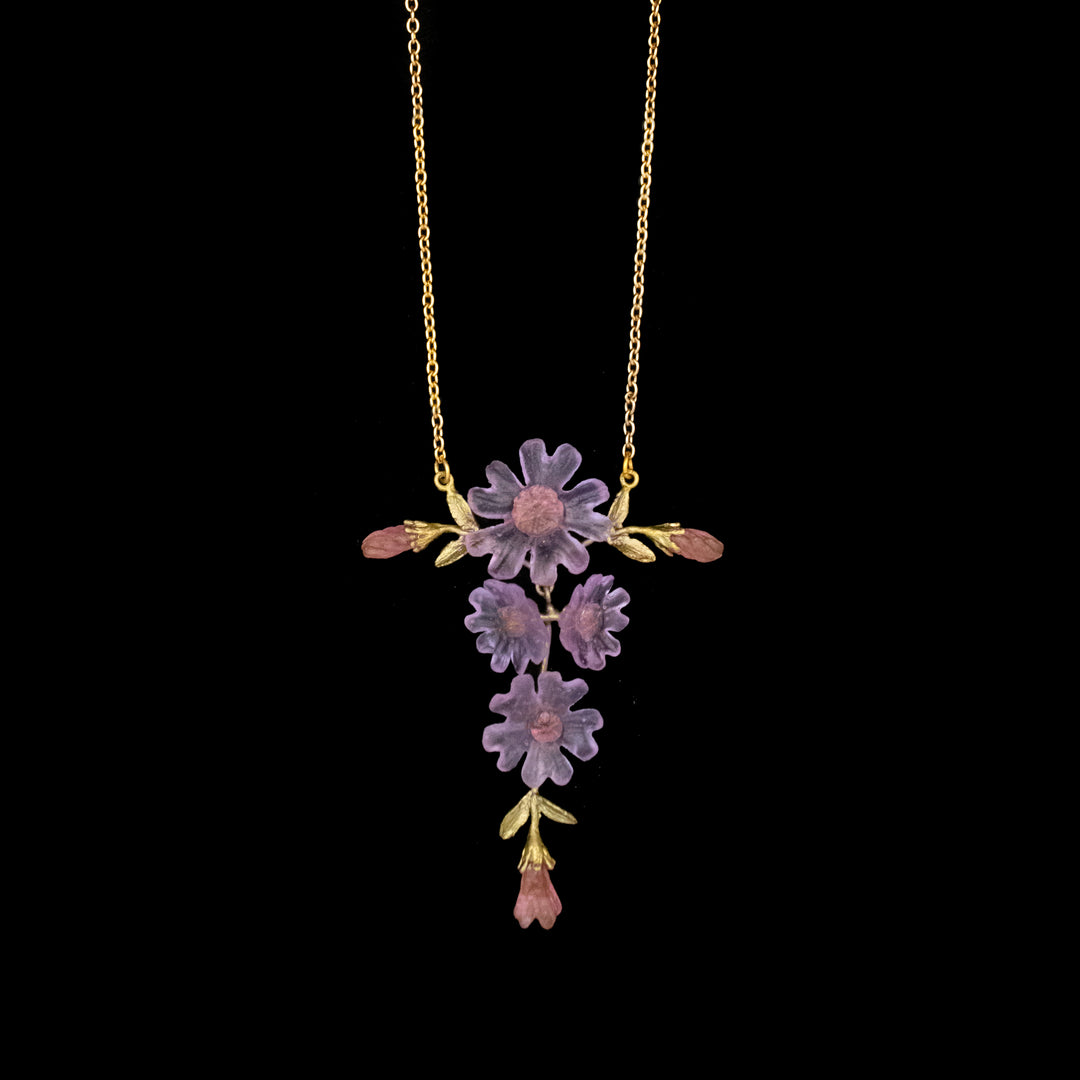 A gold necklace featuring purple and pink flower-shaped pendants with green leaf accents, displayed on a black background.