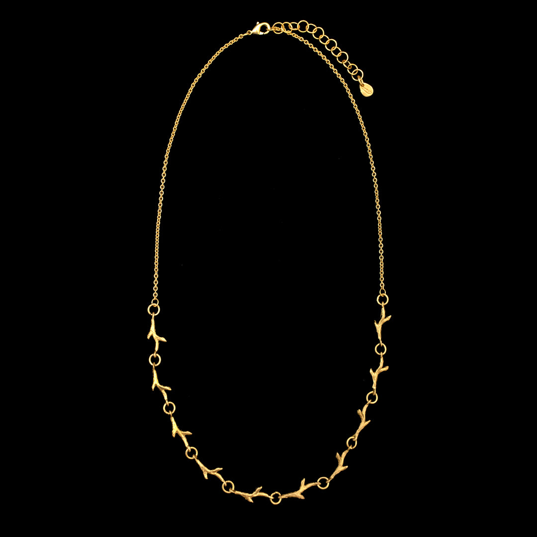 Golden necklace with a delicate chain featuring small, evenly spaced, branch-like links, displayed on a black background. This adjustable necklace offers versatility for any neckline.