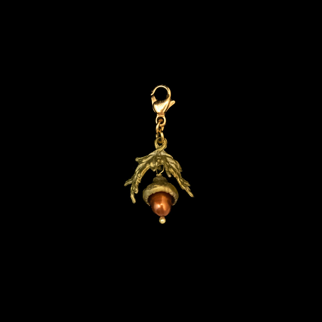 A bronze charm in the shape of an acorn with a brown freshwater pearl attached to a gold-colored clasp.