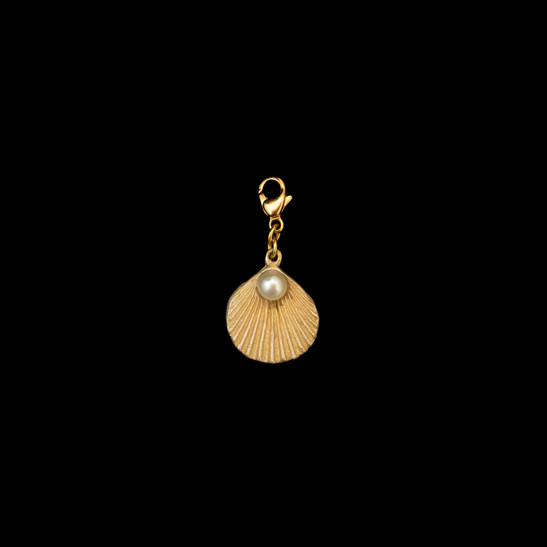 A gold-colored charm in the shape of a sea scallop shell with a freshwater pearl accent, against a black background.