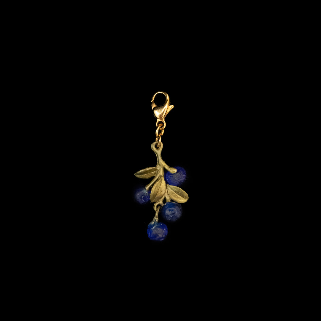 Green charm with a branch and leaves design, featuring three cast glass blueberries in rich blue, attached to a lobster clasp. This unique Blueberry charm is crafted from hand patinated bronze and shown on a black background.
