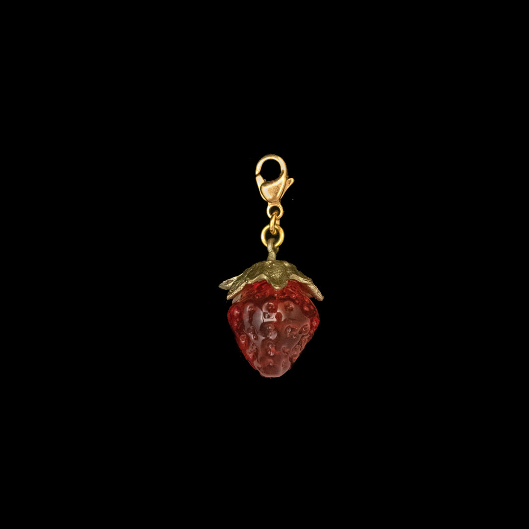 The Strawberry Charm is a cute red berry-shaped accessory with gold leaves and a gold clasp, displayed on a black background—a charming glass jewelry piece.
