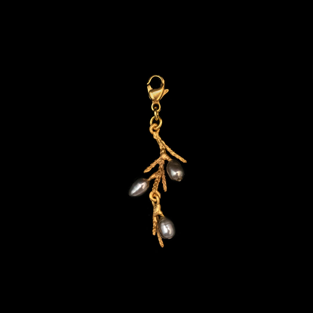Gold-plated bronze juniper charm shaped like a twig, adorned with three dark freshwater pearls, set against a solid black background.