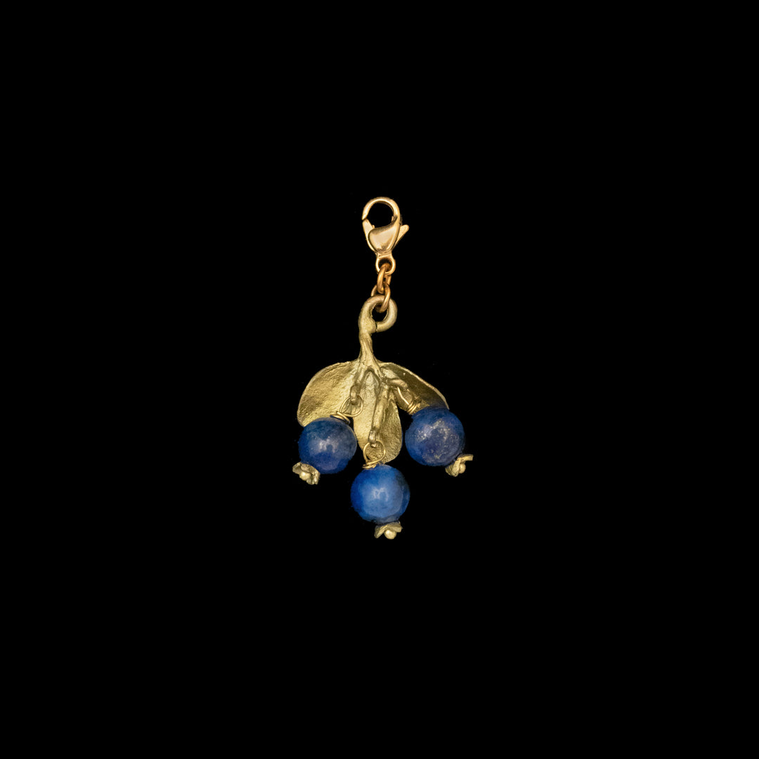 A Blueberry Charm featuring hand patinated bronze shaped like a leafy branch with three lapis lazuli beads, attached to a lobster clasp, displayed on a black background.