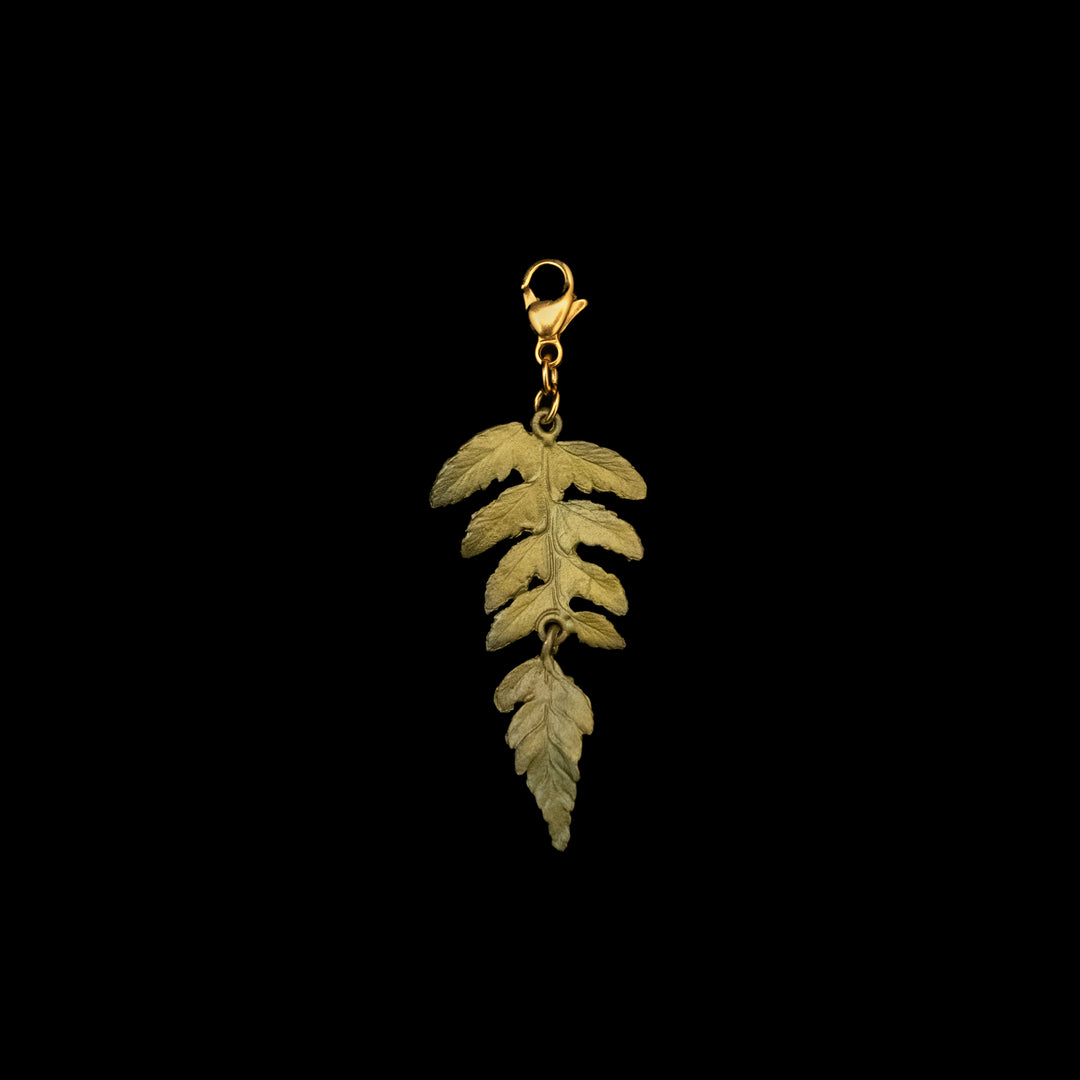 A green fern leaf charm featuring a single, intricately detailed fern leaf, hand patinated bronze pendant against a black background—an elegant piece of jewelry.