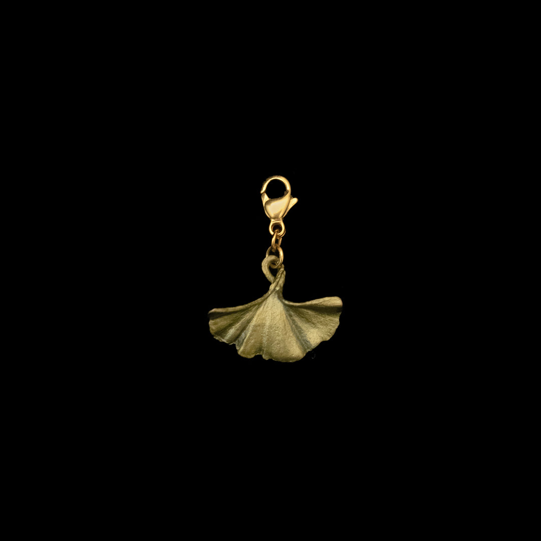 A gold clasp holds a hand patinated bronze Ginkgo Charm with a timeless design, elegantly displayed against a black background.