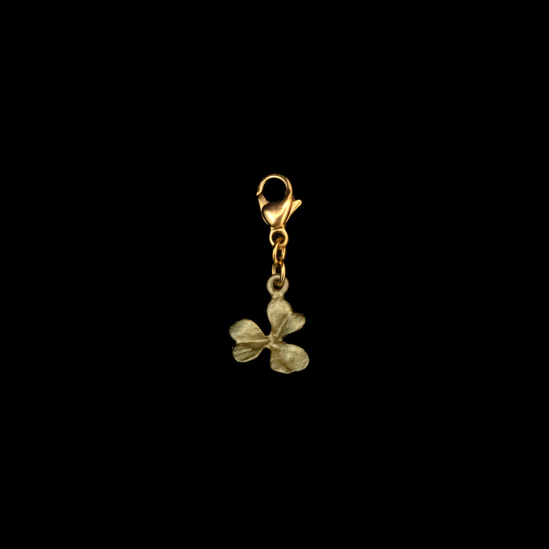 A green clover charm with a clasp and a small, three-petal flower pendant against a black background—perfect as good luck jewelry.
