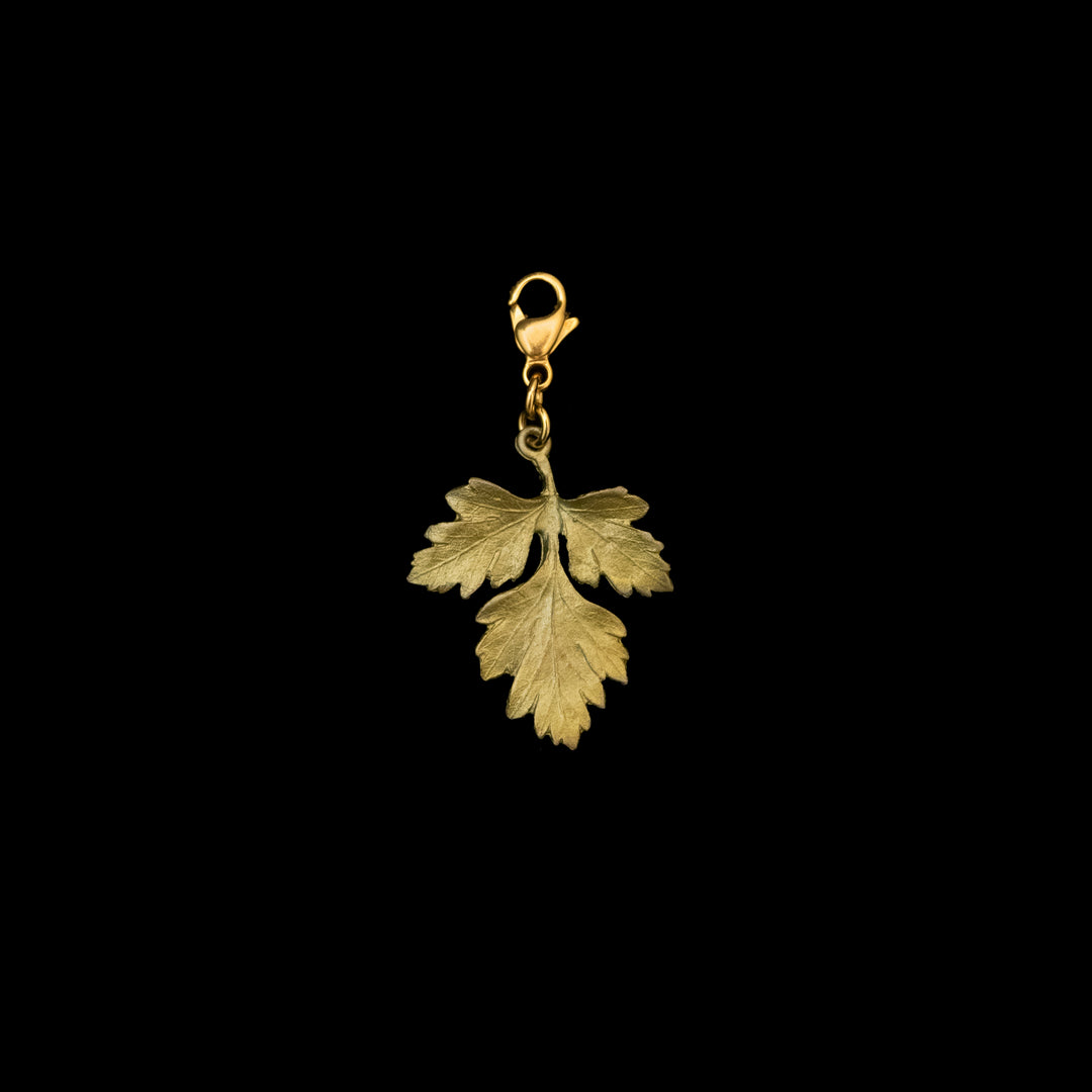 A hand patinated cast bronze charm in the shape of a parsley leaf with a clasp, isolated on a black background.