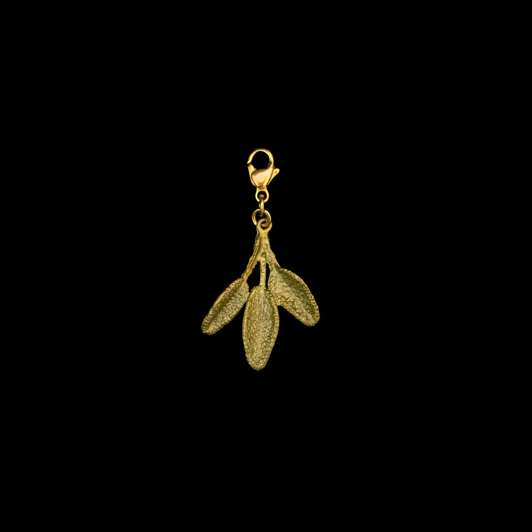 A green-colored sage charm featuring three textured, elongated oval leaves hanging from a lobster clasp, against a black background.