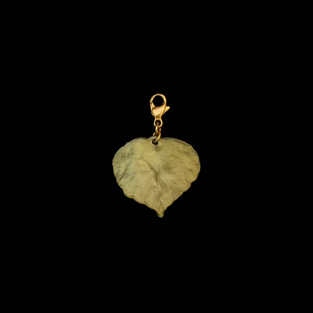 A green-toned Aspen Leaf Charm pendant, hand patinated bronze for a unique finish, features a lobster clasp and is displayed against a black background—symbolizing courage and determination.