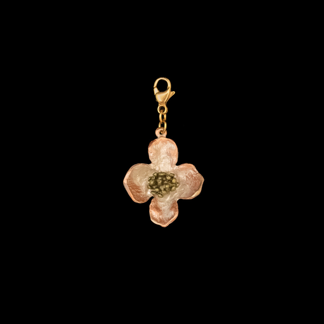 A botanical jewelry piece, this gold and copper-toned dogwood charm features textured petals and a detailed center, crafted in silver plated bronze with a lobster clasp, set against a black background.