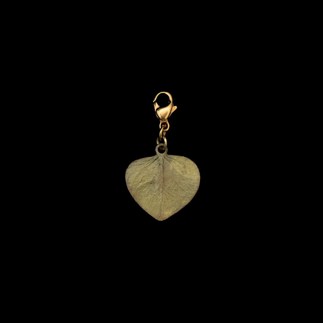 A green-colored metal charm in the shape of a eucalyptus leaf with a clasp, isolated on a black background.