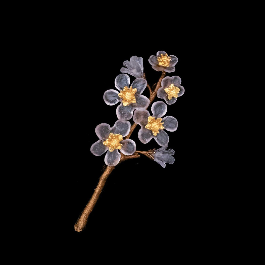 A decorative brooch shaped like a branch with translucent pale pink handcrafted glass flowers and gold centers, set against a black background—a stunning piece of floral-inspired jewelry.