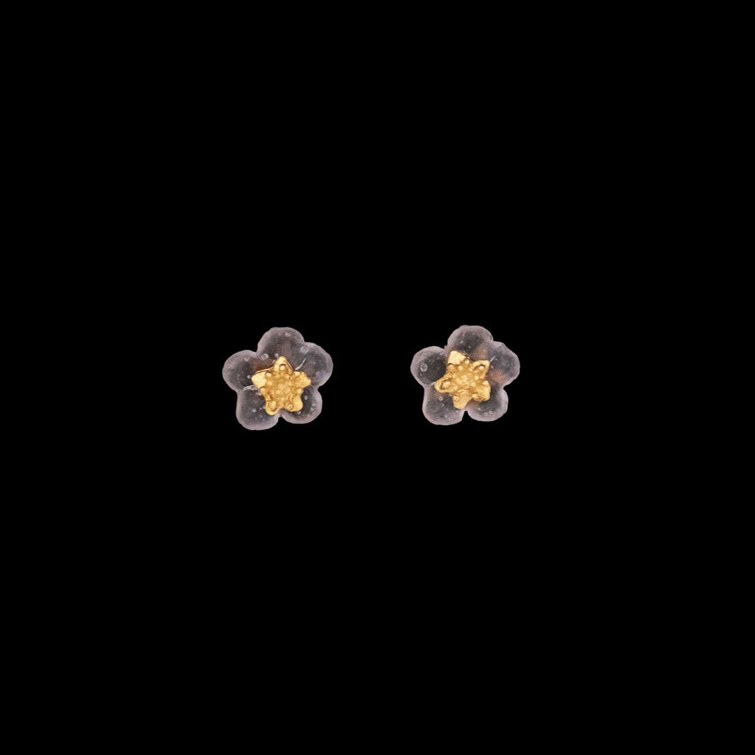 A pair of small stud earrings shaped like flowers with pale pink petals and gold-toned centers, this floral-inspired jewelry is displayed on a black background.