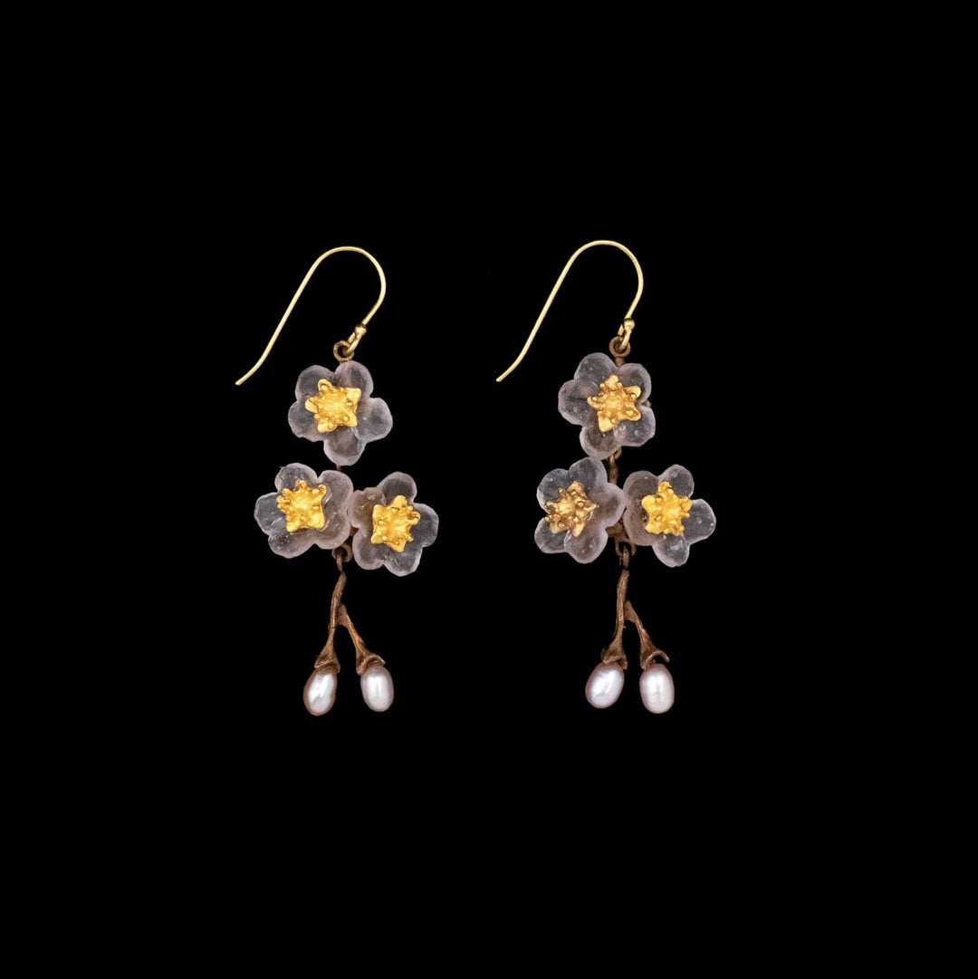 A pair of dangling earrings featuring translucent handcrafted glass flower shapes with yellow centers and small white pearls hanging from brown branches, set against a black background—ideal for floral-inspired jewelry lovers.