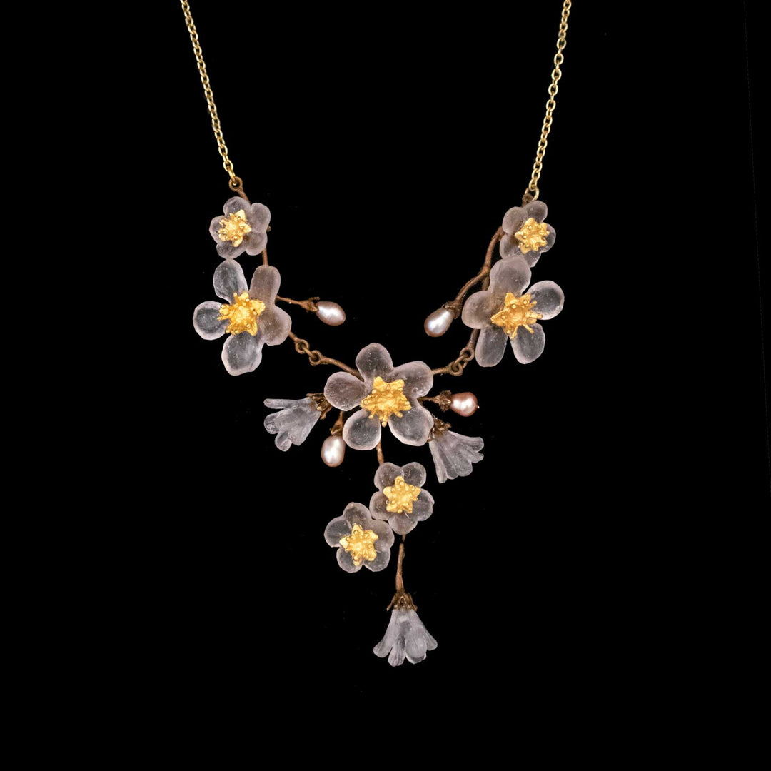 Golden chain necklace showcasing translucent, cherry blossom jewelry-inspired flower pendants with yellow centers and pearl accents, arranged in a symmetrical floral design on a black background.