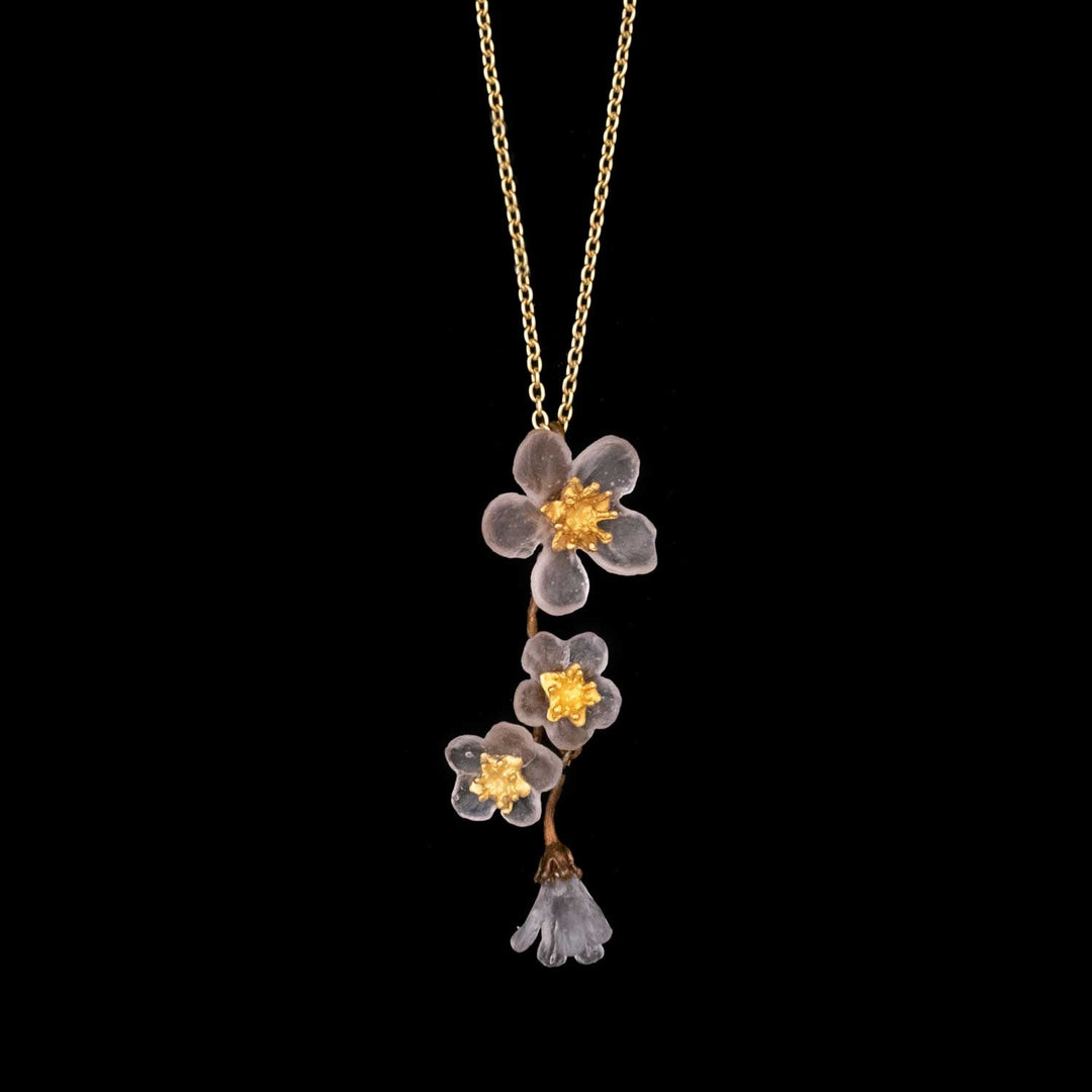 A gold chain necklace featuring a pendant with three translucent handcrafted glass flowers with gold centers, and a single translucent bell-shaped flower at the bottom, on a black background.
