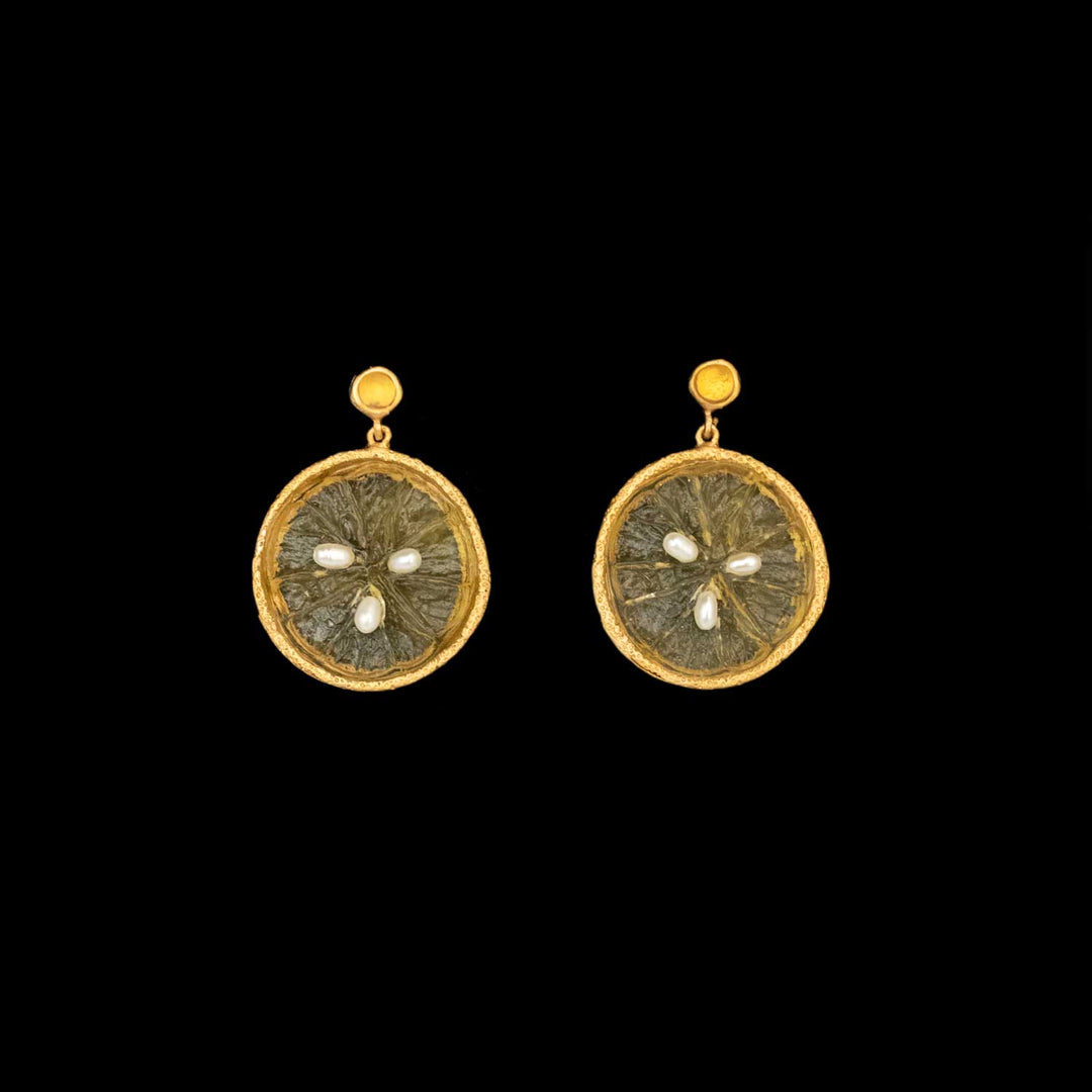A pair of round gold plated earrings with textured yellow glass centers and three small pearls arranged in a cross pattern on each earring, showcasing the charm of handmade botanical earrings against a striking black background.
