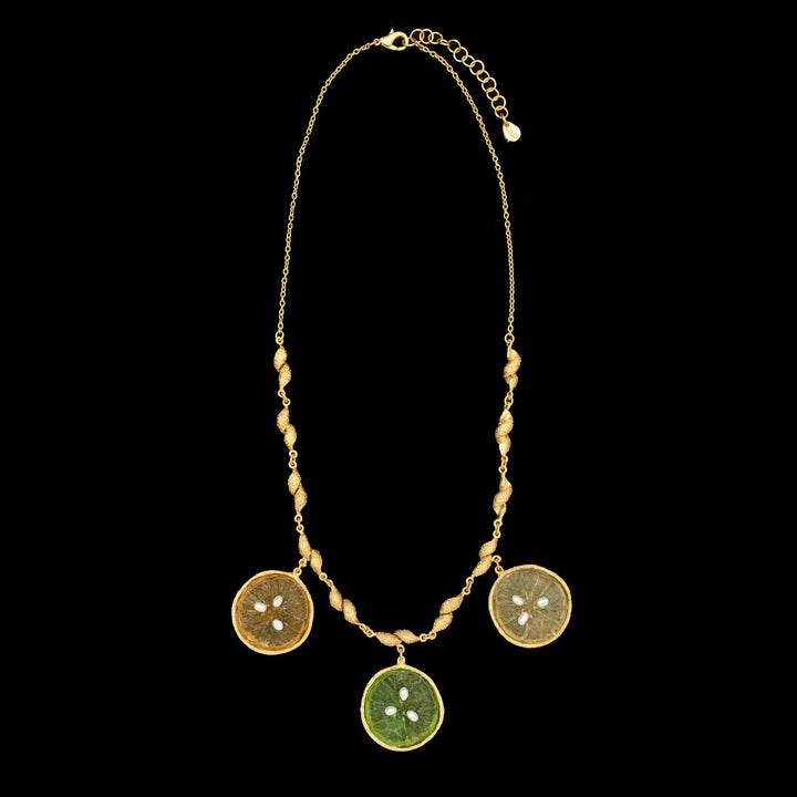 The Citrus Necklace by Michael Michaud Jewelry features three round citrus slice pendants— light yellow, orange and green—on a twisted chain, beautifully displayed against a bold black background.