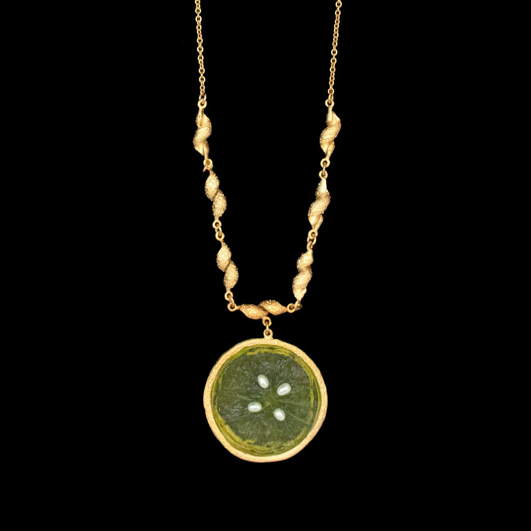 The Citrus Pendant - Large Lime features a 24kt gold-plated chain with textured links and a round lime slice pendant accented by four seeds—a striking piece from Michael Michaud Jewelry shown on a black background.