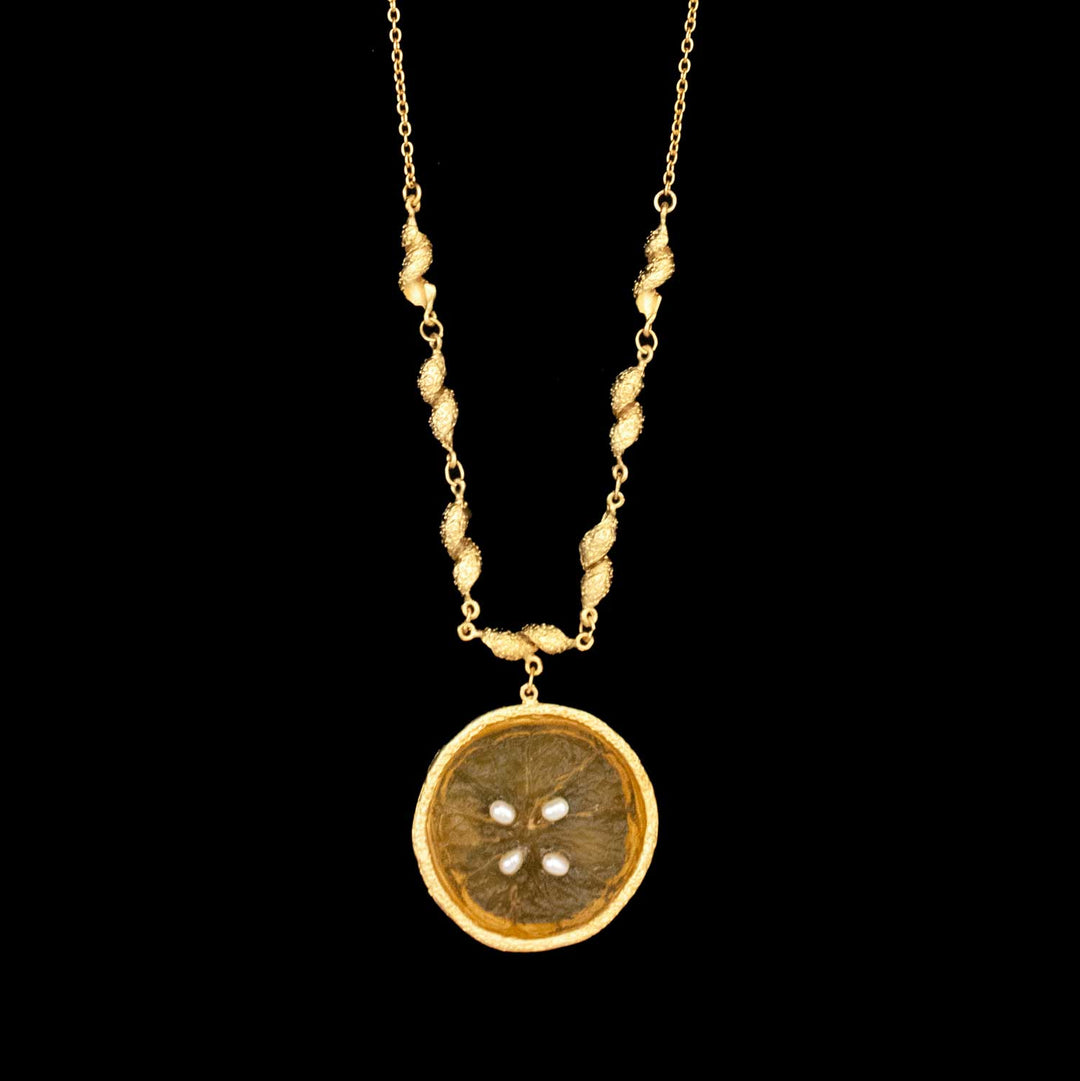 The Citrus Pendant - Large Orange features textured, twisted gold links and a circular orange pendant resembling a dried citrus slice with visible seeds, elegantly displayed on a black background.