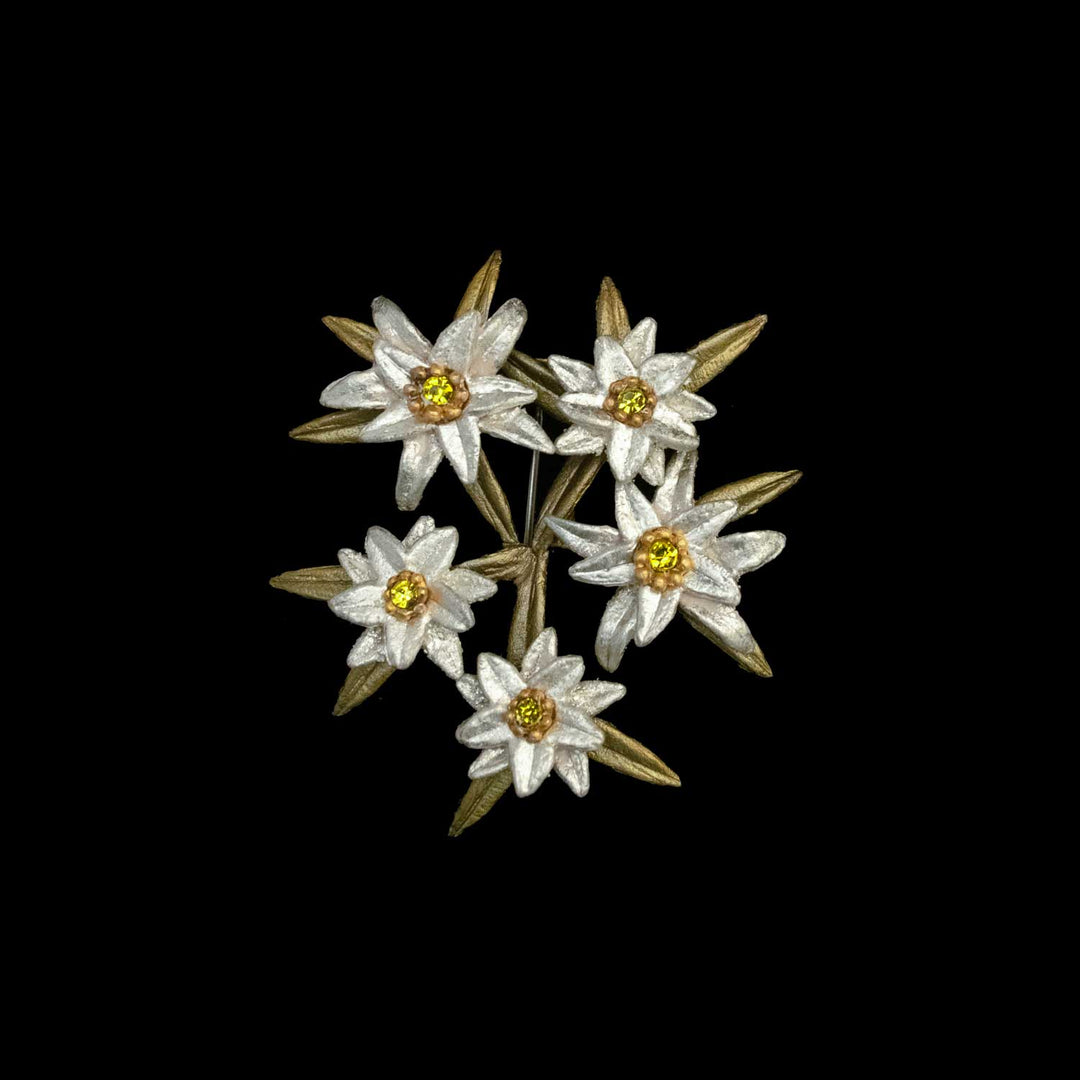 A stunning Edelweiss brooch inspired by The Sound of Music, featuring five white flowers with yellow centers and green leaves in a circular cluster, set against a black background.
