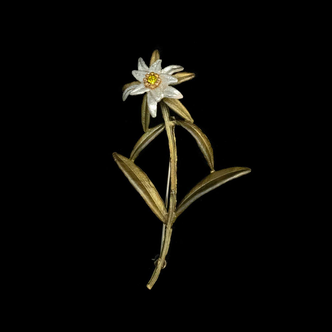 Gold and white Edelweiss brooch with green leaves and a yellow center, inspired by The Sound of Music, displayed on a black background.