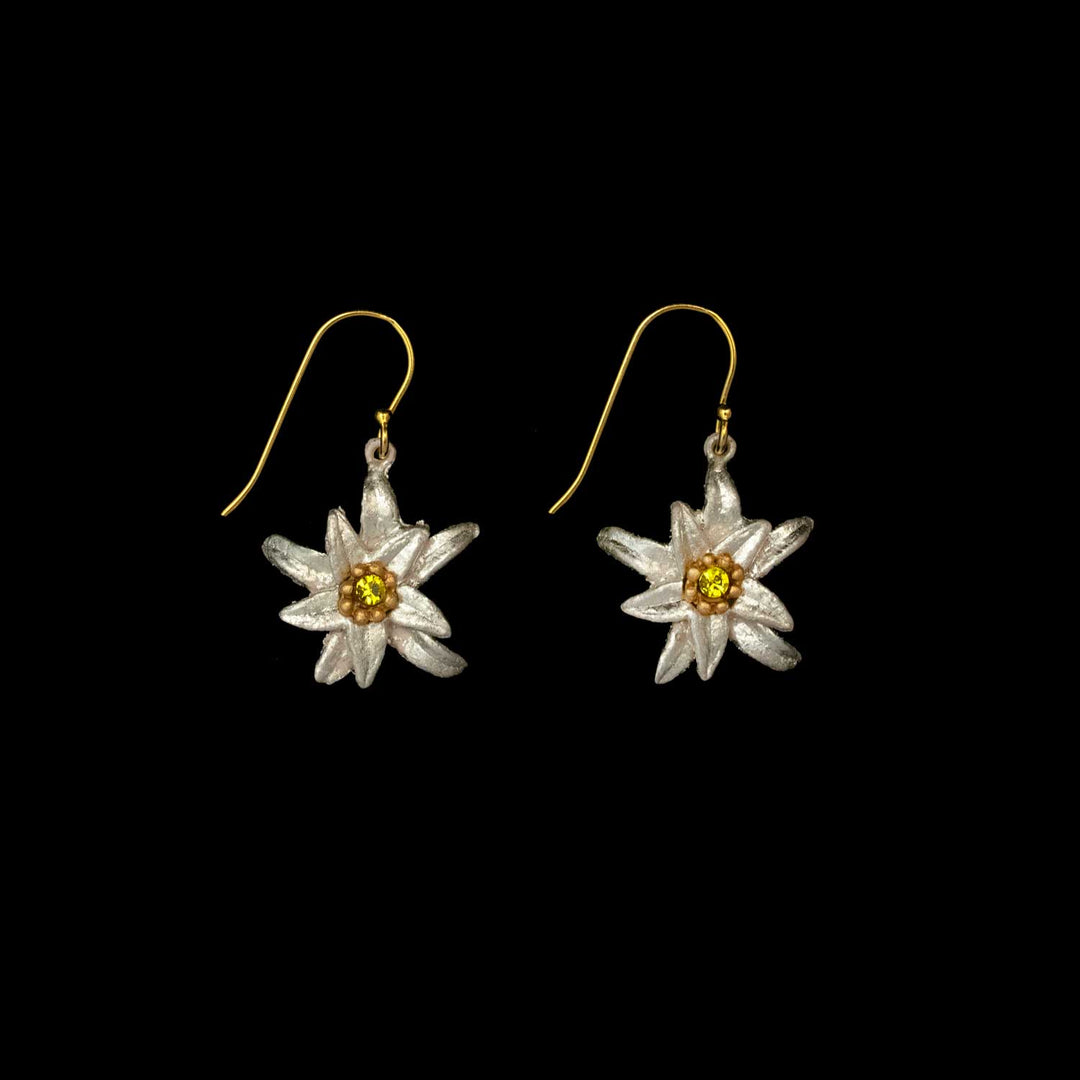 A pair of Edelweiss earrings shaped like white-petaled flowers with yellow centers, set on gold hooks and reminiscent of The Sound of Music, displayed against a black background.
