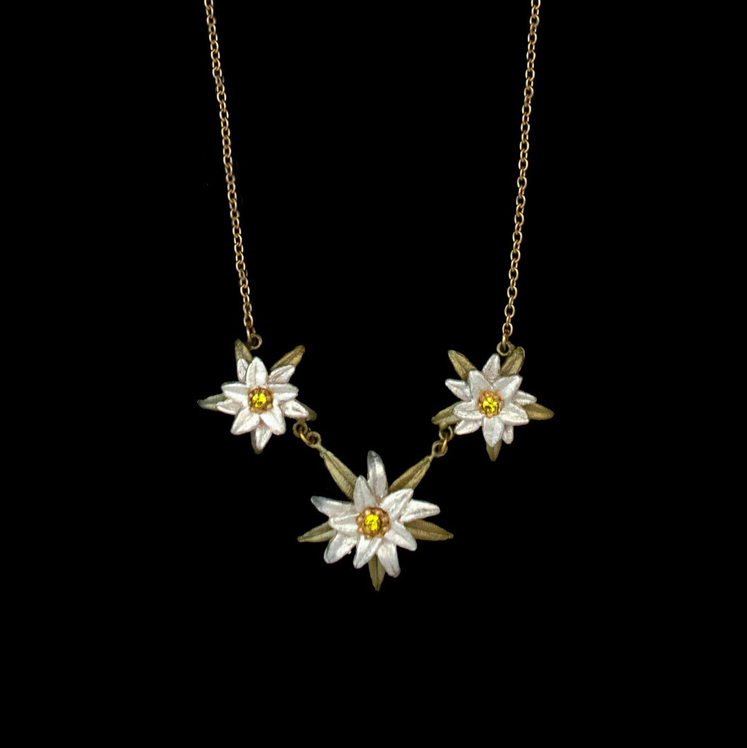Golden Edelweiss necklace with three white and yellow flower-shaped pendants, each featuring a yellow center, arranged in a row and set against a black background—a charming nod to Sound of Music jewelry.